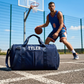 Person playing basketball with a blue duffel bag labeled 'Tyler' on an outdoor court.