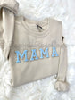 Beige sweatshirt with light blue chenille MAMA patch on white fuzzy background