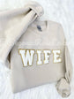 Tan crewneck sweatshirt with a white and gold wife patch