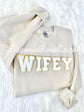Folded tan sweatshirt featuring a chenille wifey patch