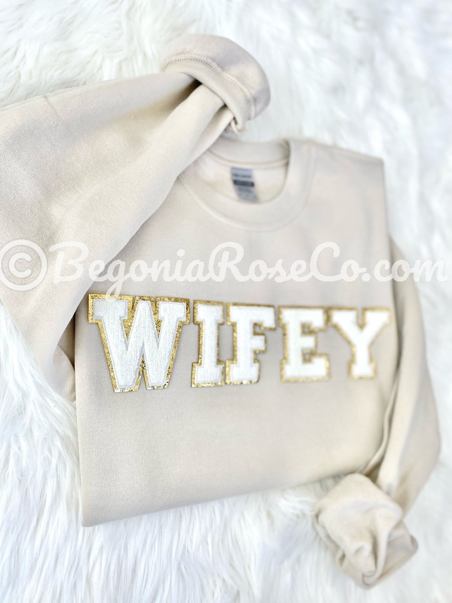Folded tan sweatshirt featuring a chenille wifey patch