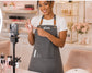 Nail artist in a gray glam apron filming a tutorial in her salon